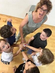 ילדים בקבוצה חברתית ואורית שמים ידיים זה על גבי זה ואומרים שלום בסוף הקבוצה החברתית