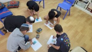 ילדים יושבים על רצפה זה לצד זה ומציירים סביב קלף כדרך להרפיה במסגרת קבוצה חברתית